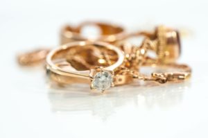 Real gold rings, chains, diamonds and gems on shiny surface, white background. Jubiler online – Coraz większa ilość złota, także biżuterii, jest sprzedawana online
